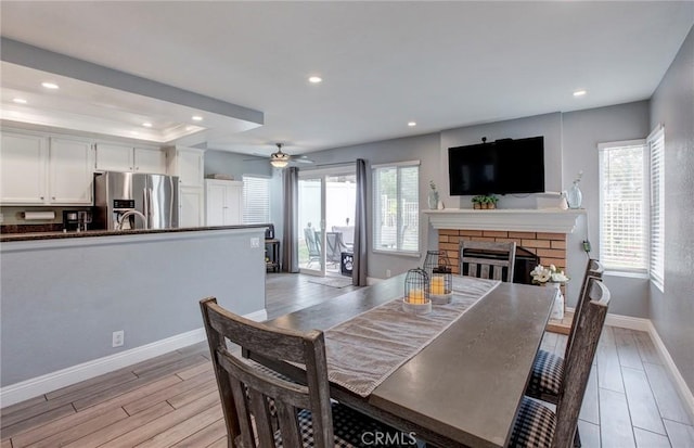 dining area with light wood-style flooring, baseboards, recessed lighting, a fireplace, and a ceiling fan