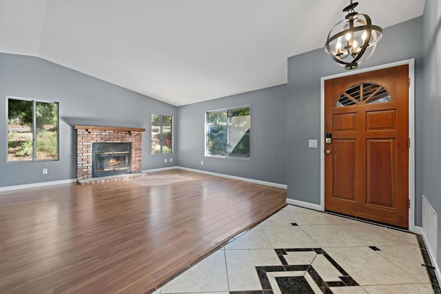 foyer featuring light wood-style floors, an inviting chandelier, a fireplace, lofted ceiling, and baseboards