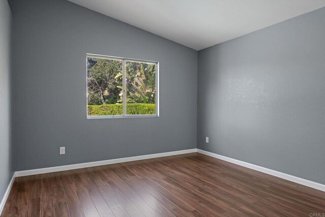 empty room with baseboards, vaulted ceiling, and dark wood-style floors