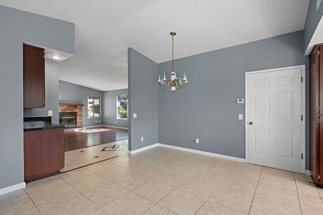 kitchen with an inviting chandelier, vaulted ceiling, light tile patterned flooring, a brick fireplace, and open floor plan