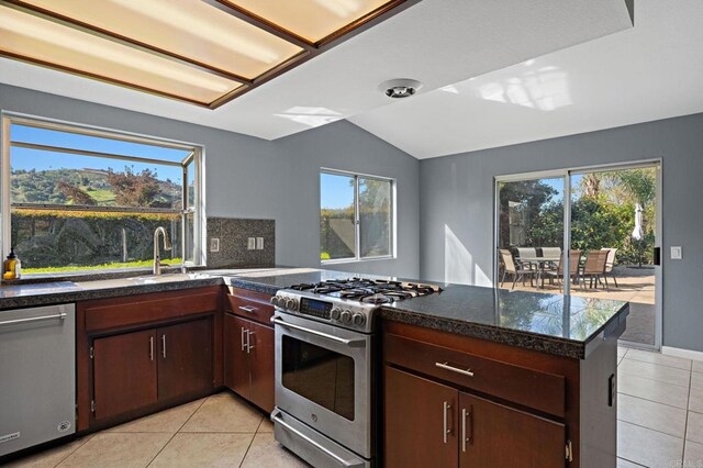 kitchen with vaulted ceiling, light tile patterned floors, a peninsula, dark countertops, and appliances with stainless steel finishes