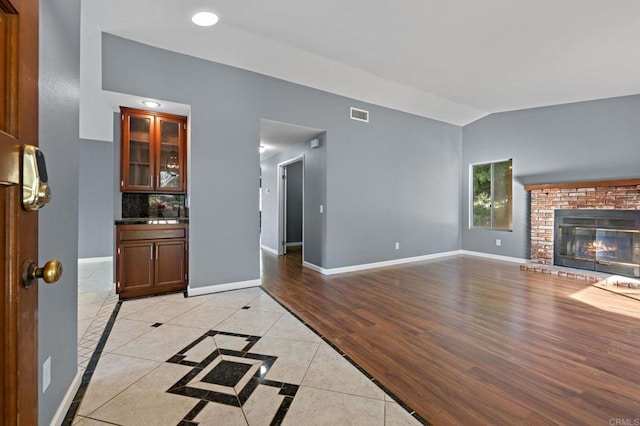 unfurnished living room with visible vents, baseboards, light tile patterned floors, a brick fireplace, and vaulted ceiling