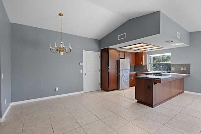 kitchen with an inviting chandelier, vaulted ceiling, a peninsula, freestanding refrigerator, and decorative backsplash