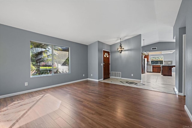 unfurnished living room with visible vents, baseboards, a notable chandelier, wood finished floors, and lofted ceiling