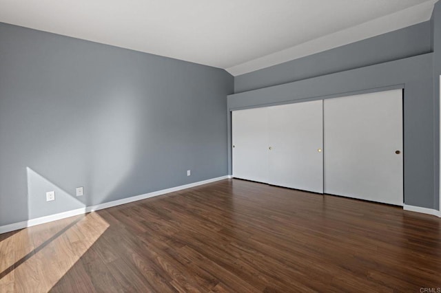 unfurnished bedroom featuring a closet, baseboards, vaulted ceiling, and wood finished floors