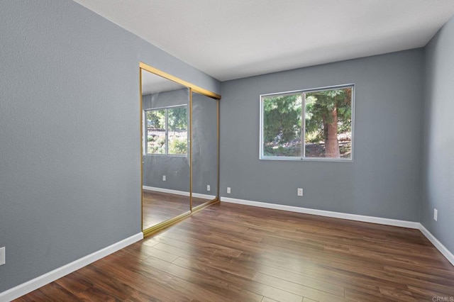 unfurnished bedroom with wood finished floors, baseboards, and a closet