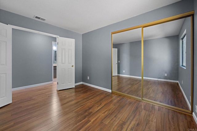 unfurnished bedroom with wood finished floors, baseboards, a closet, and visible vents