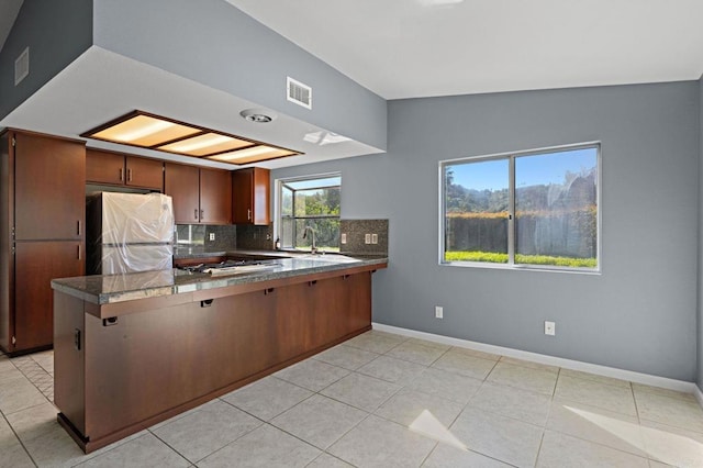 kitchen featuring baseboards, a peninsula, freestanding refrigerator, visible vents, and a sink