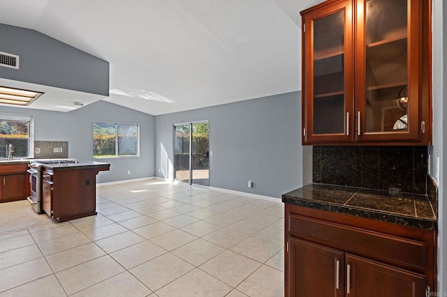 kitchen with light tile patterned floors, glass insert cabinets, high end stainless steel range oven, backsplash, and lofted ceiling