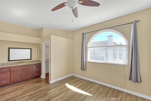 unfurnished bedroom with light wood-type flooring, baseboards, ceiling fan, and a sink