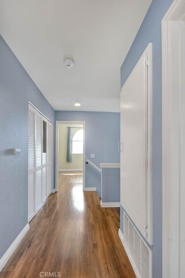 corridor featuring baseboards, an upstairs landing, visible vents, and wood finished floors