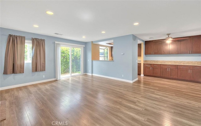 unfurnished living room with light wood finished floors, a wealth of natural light, and baseboards