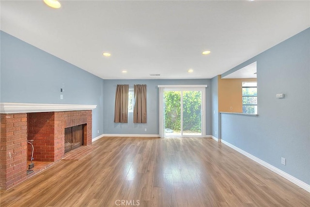 unfurnished living room featuring baseboards, a brick fireplace, and wood finished floors