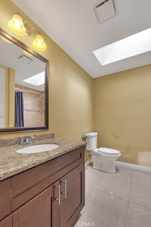 bathroom with a skylight, toilet, vanity, visible vents, and baseboards