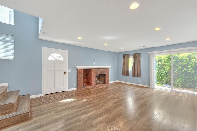 unfurnished living room featuring baseboards, wood finished floors, recessed lighting, stairway, and a brick fireplace