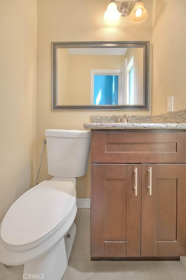 bathroom featuring tile patterned floors, toilet, vanity, and a textured wall