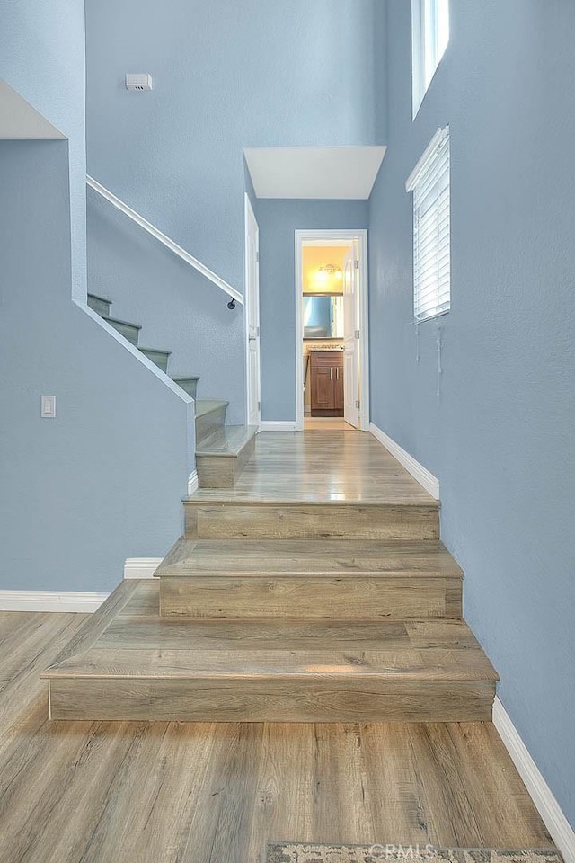 stairs with wood finished floors, baseboards, and a towering ceiling