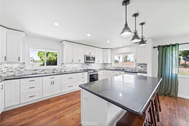 kitchen featuring dark wood-style flooring, decorative backsplash, dark countertops, and stainless steel appliances