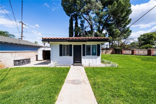 view of front of house featuring a tiled roof, board and batten siding, an outbuilding, fence, and a front lawn