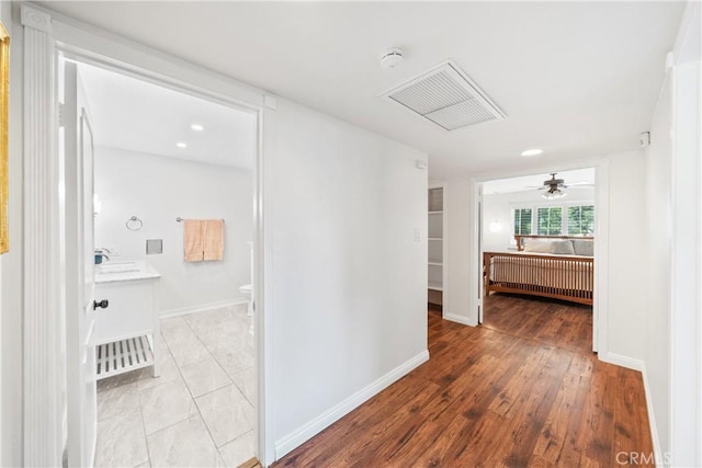 hall with light wood-type flooring, baseboards, visible vents, radiator, and a sink