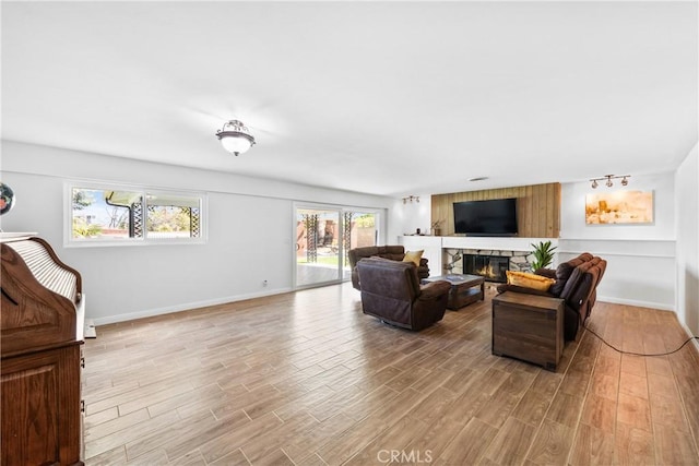 living room with light wood-style floors, a stone fireplace, and baseboards