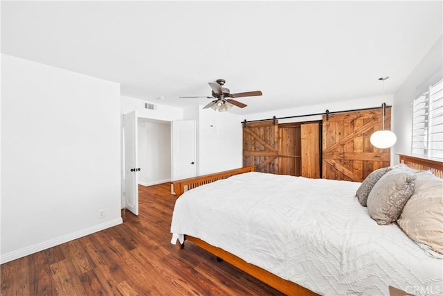 bedroom with baseboards, a barn door, visible vents, ceiling fan, and wood finished floors