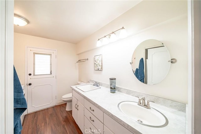 bathroom with toilet, wood finished floors, double vanity, and a sink