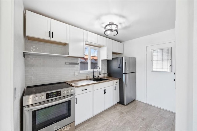 kitchen featuring white cabinets, open shelves, a sink, appliances with stainless steel finishes, and decorative backsplash