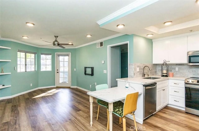 kitchen featuring a sink, light wood-type flooring, appliances with stainless steel finishes, white cabinets, and ornamental molding