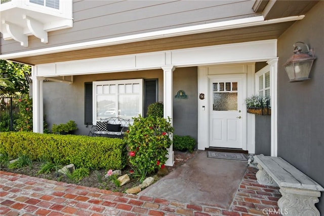 doorway to property with a porch, stucco siding, and fence