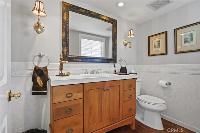 bathroom featuring vanity, visible vents, toilet, wood finished floors, and tile walls