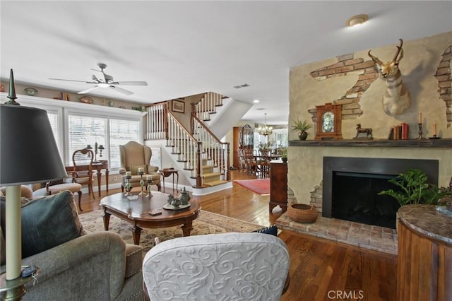 living room with visible vents, stairway, wood finished floors, and ceiling fan with notable chandelier