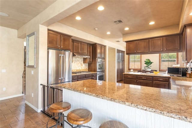30088 Mauroux Ct, Murrieta, CA 92563 - kitchen with a peninsula, visible vents, under cabinet range hood, light stone counters, and stainless steel appliances