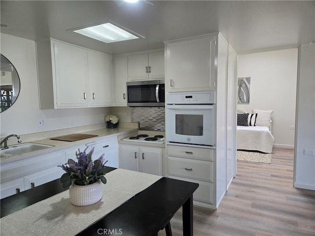 kitchen with white cabinetry, light wood finished floors, a sink, and white appliances
