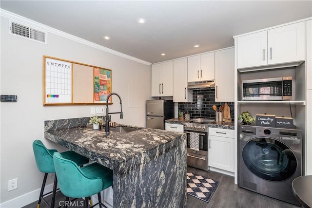 23325 La Crescenta Unit D, Mission Viejo, CA 92691 - kitchen featuring washer / clothes dryer, stainless steel appliances, a sink, under cabinet range hood, and dark wood finished floors