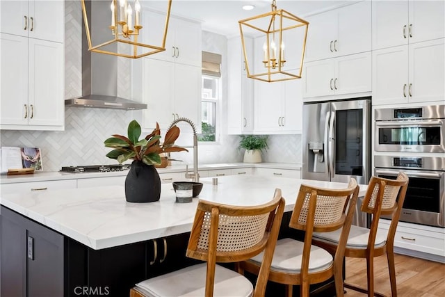 kitchen featuring an inviting chandelier, wall chimney exhaust hood, white cabinets, and stainless steel appliances