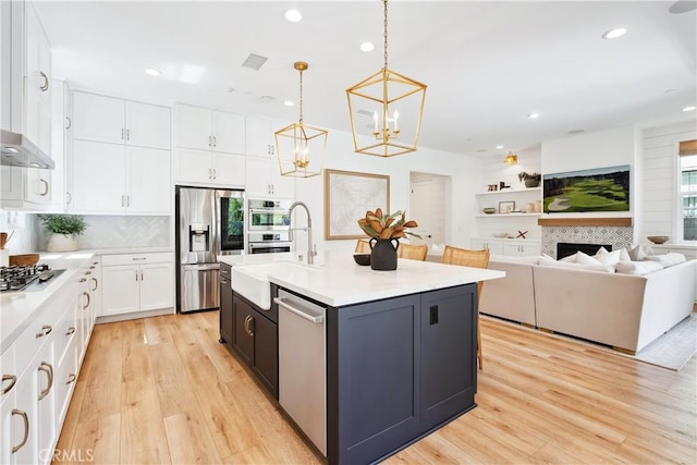 kitchen with a sink, light countertops, appliances with stainless steel finishes, white cabinetry, and light wood finished floors