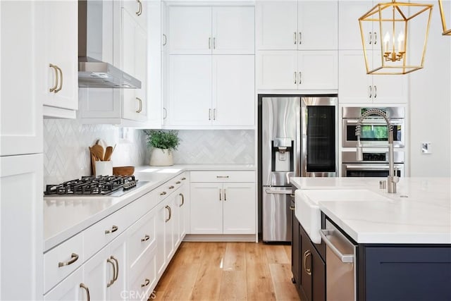 kitchen with wall chimney range hood, white cabinets, light wood-style floors, decorative backsplash, and appliances with stainless steel finishes