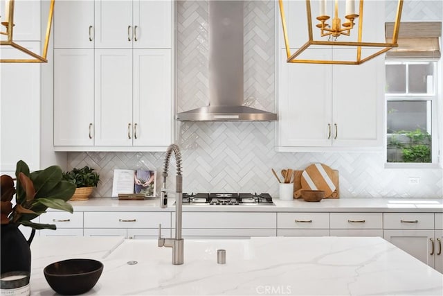 kitchen with tasteful backsplash, wall chimney range hood, white cabinets, and stainless steel gas stovetop