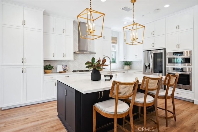 kitchen featuring an inviting chandelier, visible vents, wall chimney exhaust hood, stainless steel appliances, and a sink
