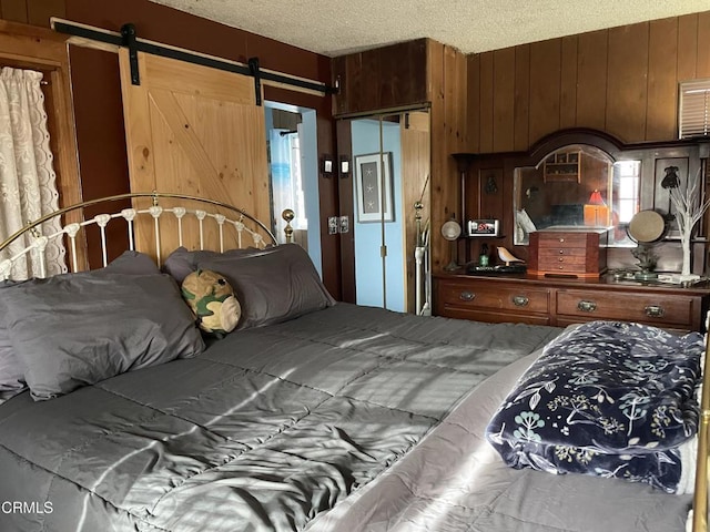 bedroom featuring wood walls, a closet, a barn door, and a textured ceiling