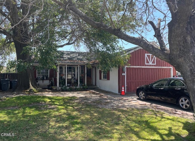 view of front facade featuring stucco siding, an outdoor structure, board and batten siding, a front yard, and a porch