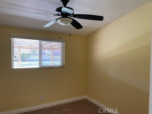 spare room with dark colored carpet, baseboards, and ceiling fan