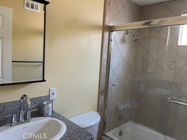 bathroom with shower / bath combination with glass door, vanity, visible vents, and toilet