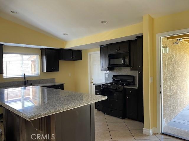kitchen featuring light tile patterned floors, black appliances, vaulted ceiling, and dark cabinets