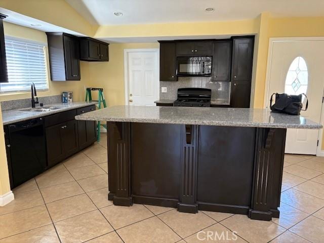 kitchen featuring light tile patterned floors, a center island, a sink, black appliances, and light stone counters