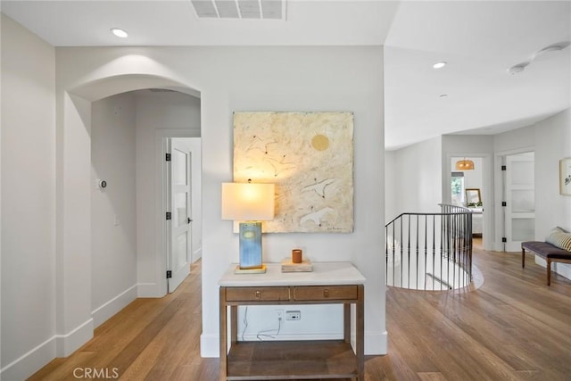 corridor with recessed lighting, an upstairs landing, visible vents, arched walkways, and wood finished floors