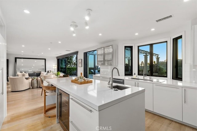 kitchen with wine cooler, an island with sink, a sink, and visible vents