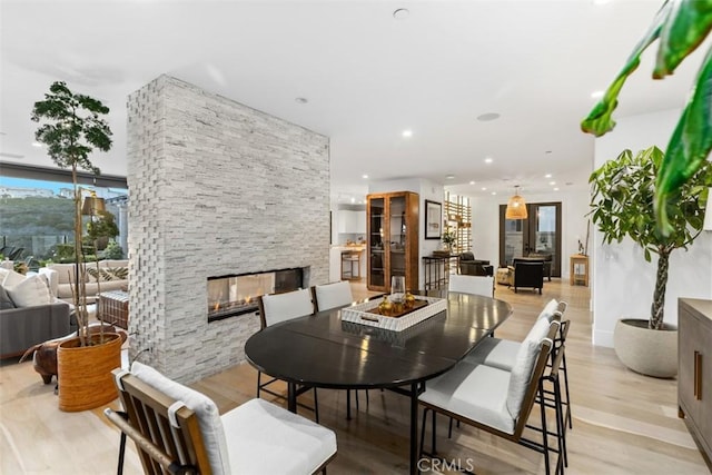 dining area featuring recessed lighting, light wood-type flooring, and a stone fireplace
