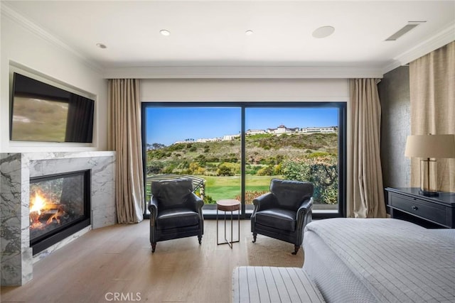 bedroom with visible vents, a premium fireplace, ornamental molding, and wood finished floors